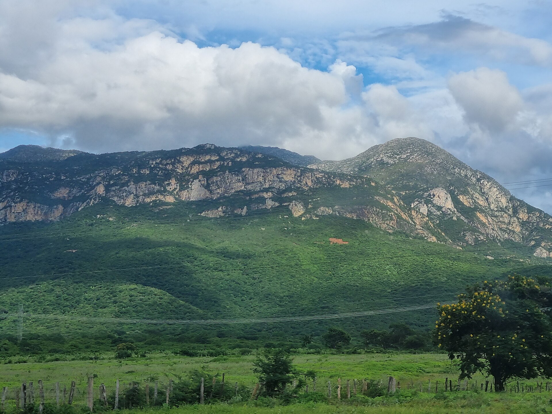 Serra rochosa entre Monte Azul e Mato Verde, com campo verde, cerca e árvore em primeiro plano.